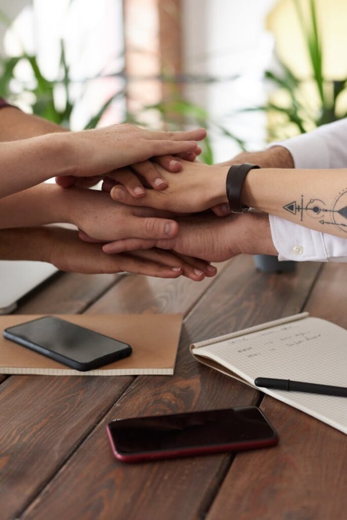 pexels photo 3184431 Hands from a diverse team stack on a table symbolizing unity and teamwork in a modern office setting.